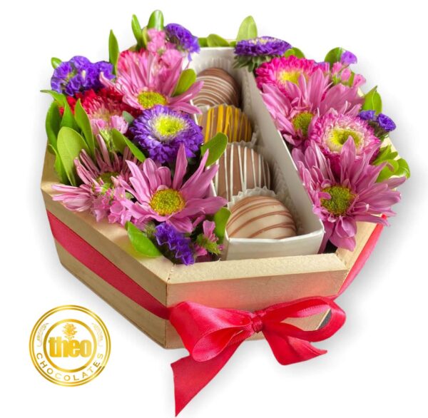 Caja con 4 bombones de chocolate y alrededor un arreglo de flores primaverales sobre una base de madera